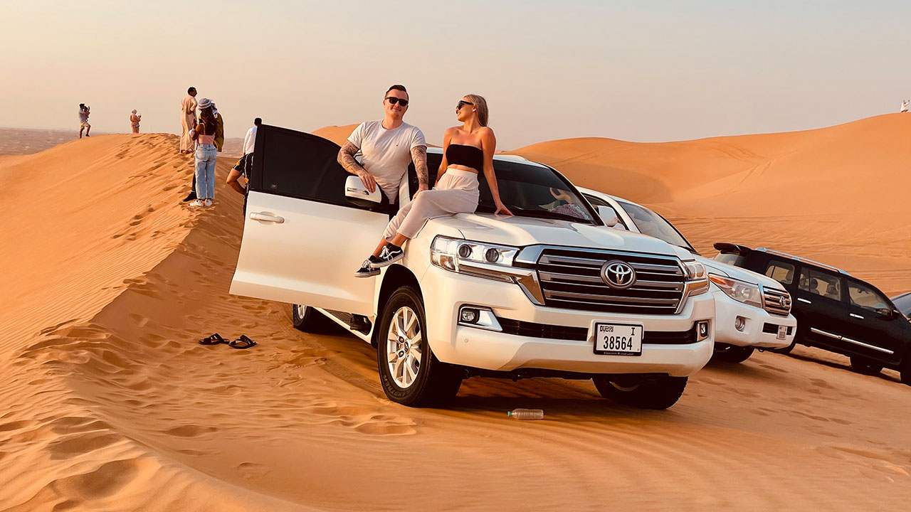 Family enjoying a morning desert safari with a white SUV on golden sand dunes, capturing scenic views and adventure moments in the desert.